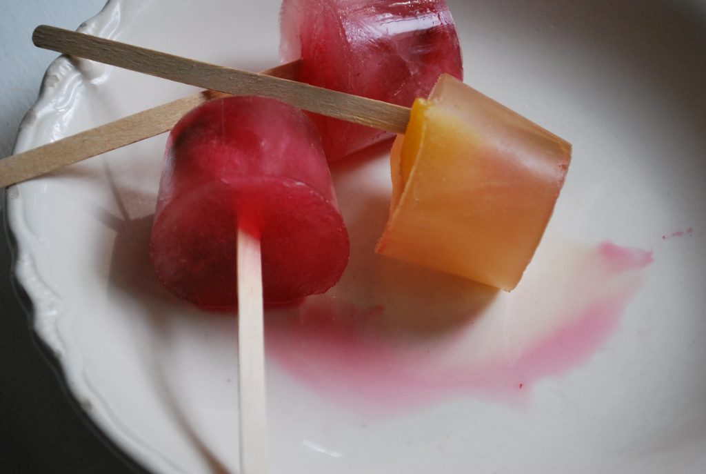 Frozen pink and yellow ice pops made from peaches and raspberries. 